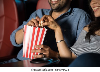 Man touching the hand of his date while grabbing some popcorn at the movie theater - Powered by Shutterstock