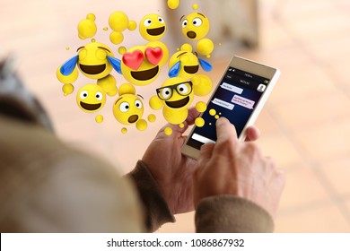 man touching the screen of his smartphone to send emoticons. All screen graphics are made up.