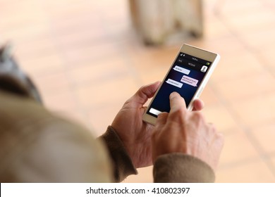 Man Touching The Screen Of His Smartphone Showing Instant Messaging App. All Screen Graphics Are Made Up.