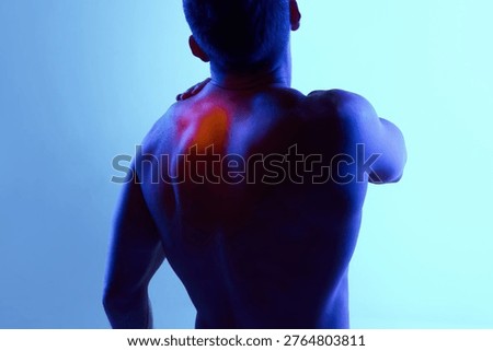Man touching upper back with red pain highlight under blue neon lighting. Concept of localized muscle tension, trigger points, posture imbalance and physiotherapy treatment needs