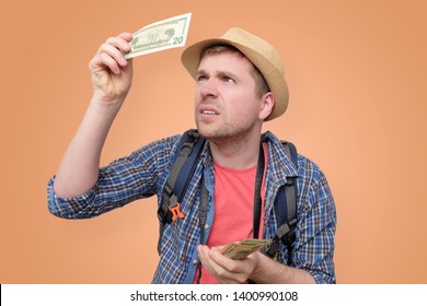 A Man Tourist In Hat Holds Dollar Bank Note Checking It For Watermark. See Through Money. Verification Of Bills On Vacation Travelling.