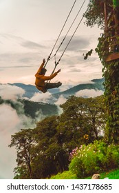 Man Tourist Having Fun Swinging On Giant Swing In Casa Del Arbol Attraction. View Of Green Mountains And Trees In Background. Wooden Treehouse. Shot In Banos, Ecuador