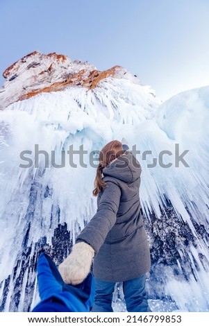 Man tourist holds girl hand against backdrop of ice cave grotto, frozen waterfall or lake.