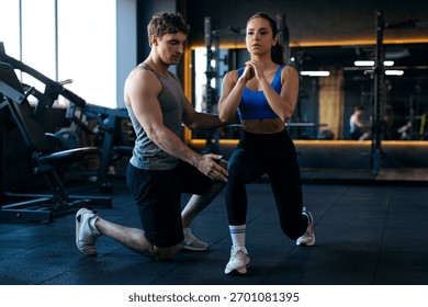 Man trainer controlling how to do lunges correctly, woman training kneeling in modern gym interior