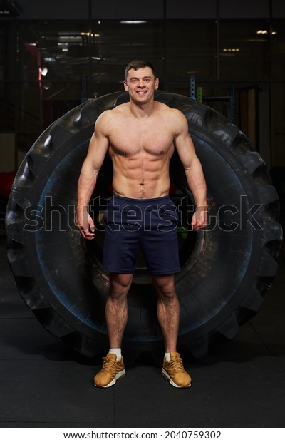 a\
man in training in the gym with a naked inflated torso stands in\
front of a huge car tire strength exercises in the\
gym