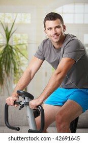 Man Training On Exercise Bike At Home, Listening Music.