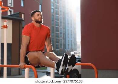 Man training on parallel bars at outdoor gym on sunny day