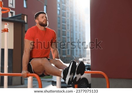 Man training on parallel bars at outdoor gym on sunny day