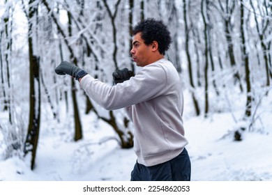 man trains boxing in winter by conducting shadow fight outdoors, in background snow covered forest - Shutterstock ID 2254862053