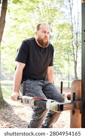 Man trains on parallel bars at outdoor gym in park and exhales with effort. Vertical fitness scene for bodyweight exercise, strength building, endurance, or active lifestyle promotion