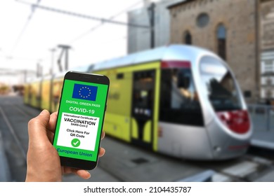 A man at a tram stop is holding smartphone with the European Union digital Green Pass for Covid-19 SARS-CoV-2. Safe travel concept during the Coronavirus pandemic and the Green Pass.
