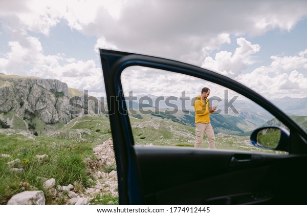 man travel by car and using smartphone in mountains on\
vacation trip. Holiday maker male relax on road trip by car to\
mountains and browsing smartphone. Tourist making browsing phone\
and gps. 
