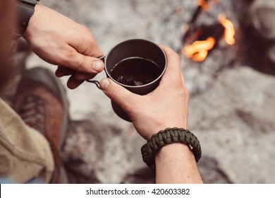 Man traveler hands holding cup of tea near the fire outdoors. Adventure, travel, tourism and camping concept. Hiker drinking tea from mug at camp. Coffee cooked over a campfire on the nature. - Powered by Shutterstock