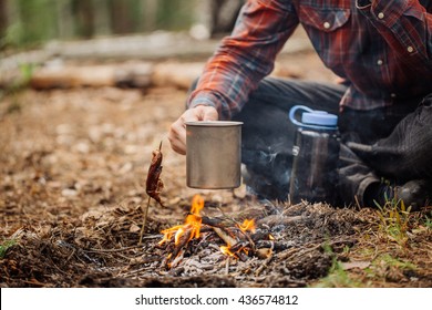 man traveler hands holding mug with water near the fire outdoors. bushcraft, adventure, travel, tourism and camping concept. - Powered by Shutterstock