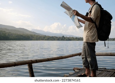 Man traveler holding map standing near lake with admiring picturesque scenery of mountainous. 