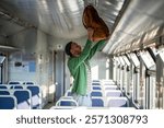 Man traveler lifts backpack onto overhead luggage rack in train, settling in for long solo journey. Public transport, solo adventure, backpacking, transit convenience, seat arrangement, railway travel