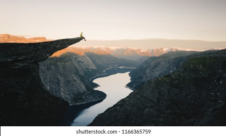 Man traveler on Trolltunga rocky cliff edge in Norway mountains Travel Lifestyle adventure emotional concept extreme vacations outdoor sunrise, tourist sitting alone - Powered by Shutterstock