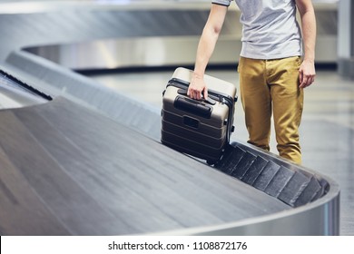 Man (traveler) Picking Up Suitcase From Baggage Claim In Airport Terminal.