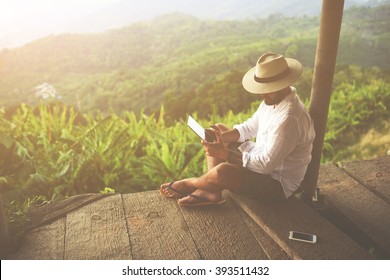 Man traveler is reading electronic book on portable touch pad, while is relaxing in the fresh air during trip in Asia.Male freelancer is working on digital tablet, while is sitting against jungle view - Powered by Shutterstock