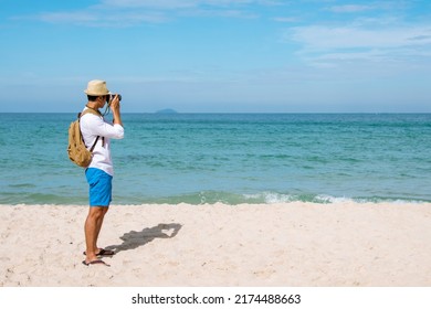 Man Traveler Using Digital Camera On Summer Beach Blue Sky Take A Photo. Asian Photographer Man Journey Relax On The Beach In Summertime. Man Backpack Shooting Photo Asia Destination Holiday Trip