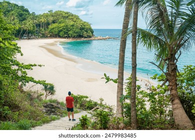 Man traveler walks down stone steps path leading to tropical sandy beach with turquoise water ocean. Male tourist standing above Freedom beach in Phuket island, Thailand with nobody - Powered by Shutterstock