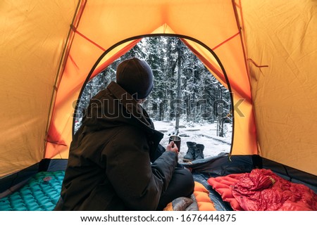 Man traveler wearing winter coat with sitting and holding a coffee cup in orange tent on campsite at Yoho national park