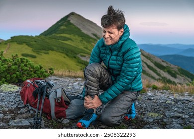 Man is Traveling with Backpack and has Problems with Sprained Ankle in the Mountains. Man with ankle injury feels pain in leg with an expression of pain on his face.