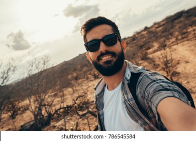 Man Traveling With Backpack Hiking In Desert. Travel Lifestyle Success Concept. Man Doing Self Portrait