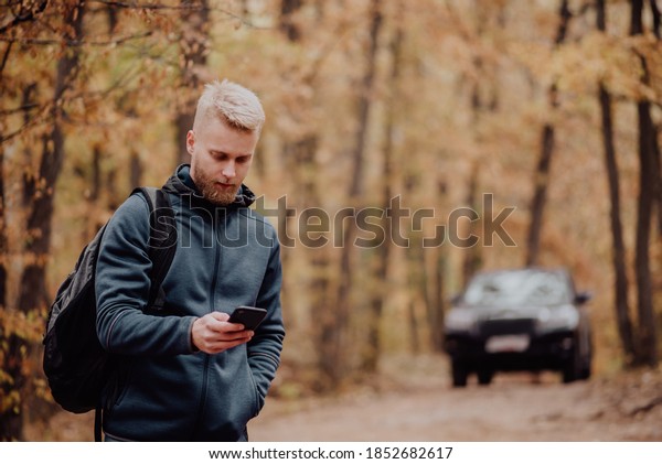 The man travels by car. The guy on the phone\
looks at where he is on the navigator. Hiker lost in the autumn\
forest concept.