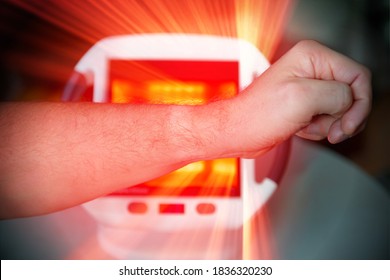 Man treating pain in the hand with infrared light therapy. The man sits at the table near the healing lamp.