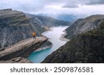 Man trekker dressed bright orange jacket enjoying glacier Ringedalsvatnet lake rose arms UP from famous Trolltunga "Troll