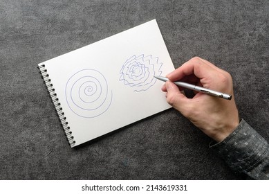 A man with trembling hands is trying to repeat the spiral drawing in a notebook. Test for essential tremor and parkinson's disease. - Shutterstock ID 2143619331