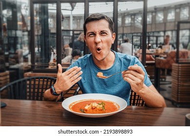 A man tries a spicy and hot red soup in a restaurant and reacts funny emotionally. Seasonings in the national cuisine and an unhealthy diet with overabundance of pepper