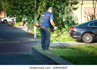 Man With Trimmer For Cutting Grass, Mowing Grass In Action, Lown Care City Service. Landscaper, Elderly Gardener Cutting Grass. Lawn Mowing Services, Worker In Personal Protective Equipment Cut Grass 