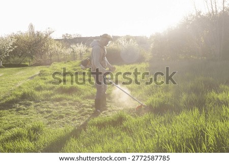 Man Trimming Grass With String Trimmer in Countryside Yard – Spring Work and Lifestyle Concept