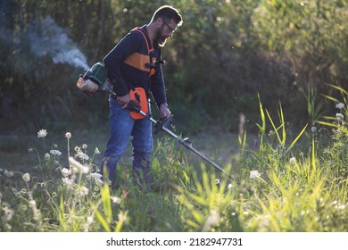 Man Trimming Weed With Weed Trimmer In Summer