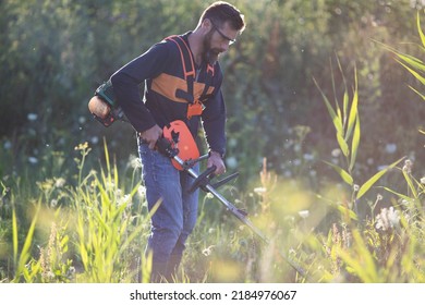 Man Trimming Weed With Weed Trimmer In Summer