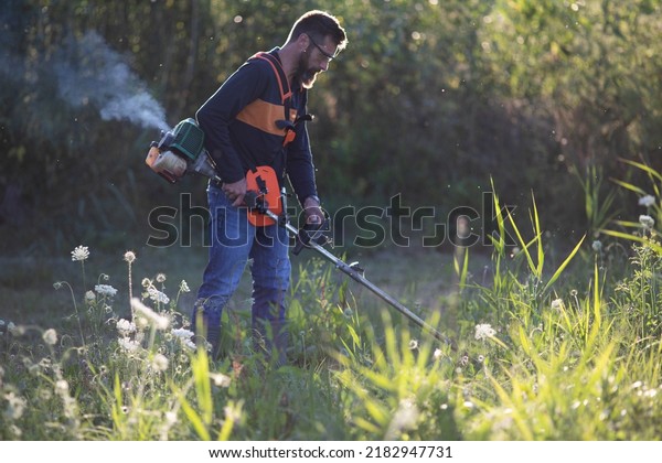 man trimming\
weed with weed trimmer in\
summer