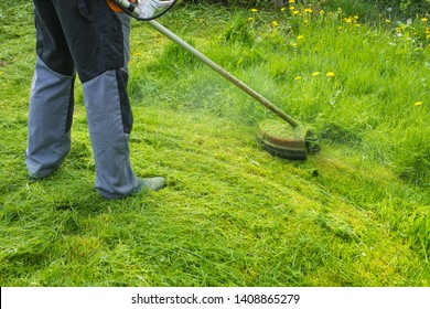 Man trims overgrown grass by grass cutter. Gas mower. Close up.