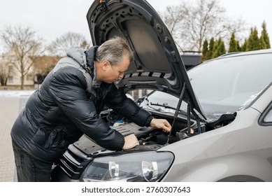 Man troubleshooting car engine under hood during winter