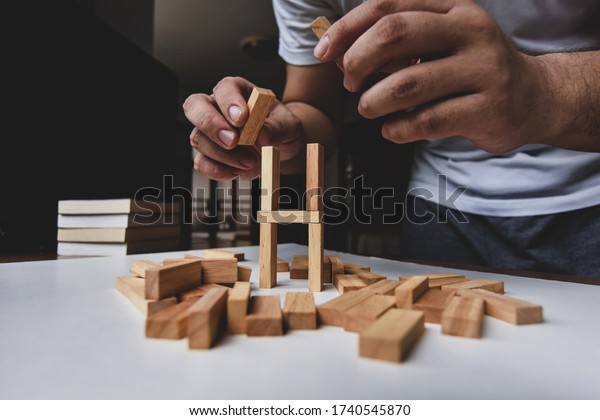A man try to rebuild wooden blocks tower\
after them breakdown on white table\
