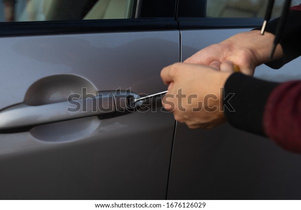 A man is trying to break the car lock in\
order to steal it from the parking\
lot.
