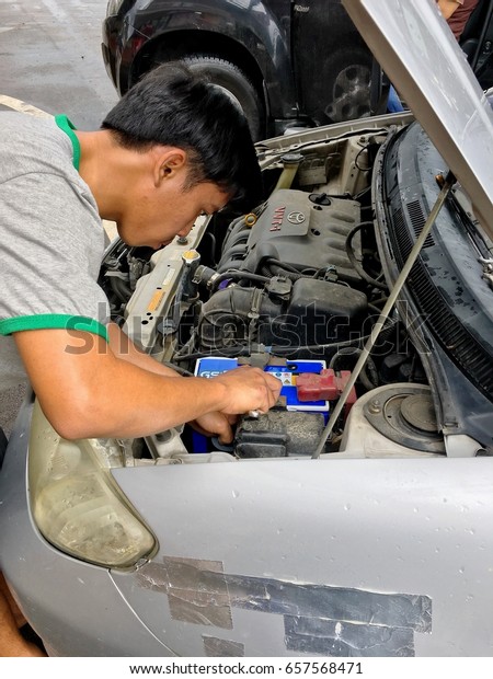 A man is trying to change the car\'s battery.\
Bangkok, Thailand June 5,2017