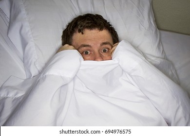 Man trying to hide himself under the covers in bed - Shutterstock ID 694976575
