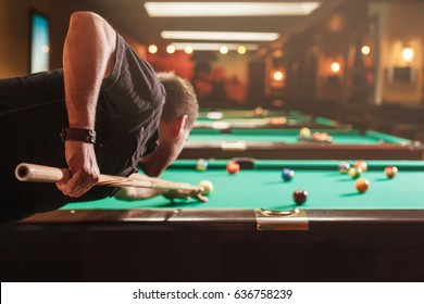 Man trying to hit the ball in billiard. Billiard room on the background.