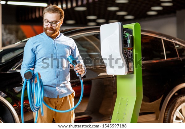Man trying a new charging cable with a car charging\
station at the car dealership. Concept of buying electric charging\
for car