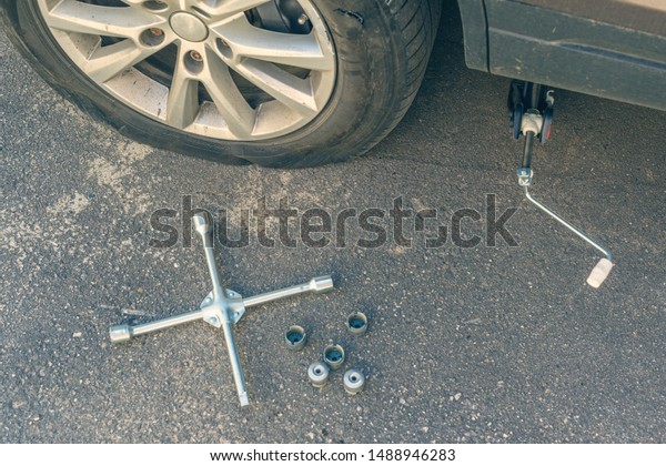 A\
man trying to twist off the bolt by his foot  using cross wrench\
for changing punctured wheel. Hole in the tire.\
Concept