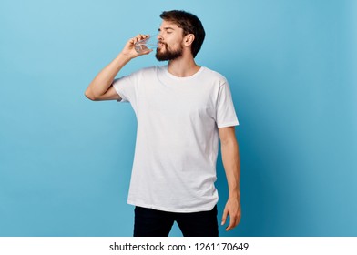 A man in a t-shirt and trousers on a blue background drinking water from a glass            - Shutterstock ID 1261170649