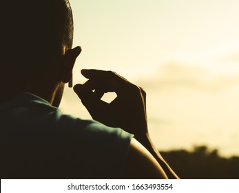 The man turned his back, wearing a blue shirt. Raising hands to hold on to the headphones With a background of wood and sky Evening atmosphere