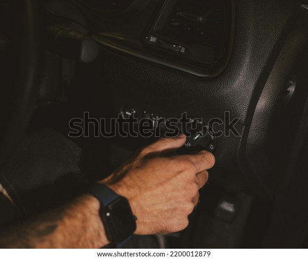 The man turns on the\
headlights in the car. The driver turns on the car\'s headlights.\
Travel by car. Close-up view with selective focus. Turning on the\
light switch.
